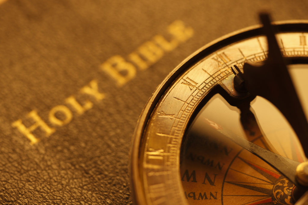 Close-up of a compass resting on a textured surface with the words 'Holy Bible' in the background representing spiritual direction services.