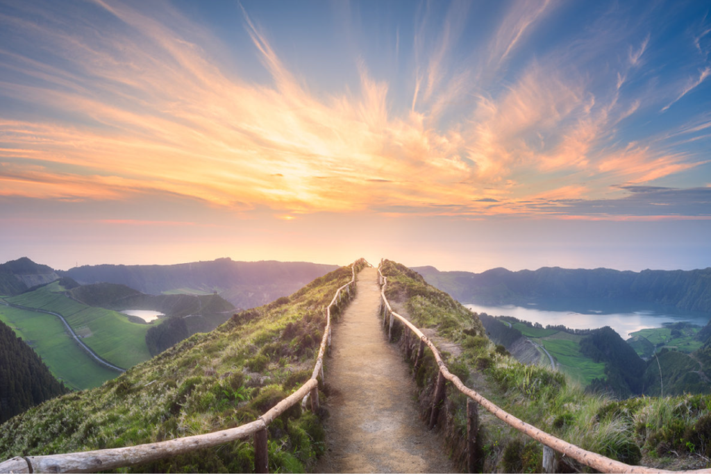 A scenic pathway leading toward a horizon during sunset, surrounded by lush hills and a lake in the distance. The image is associated with retreat services.